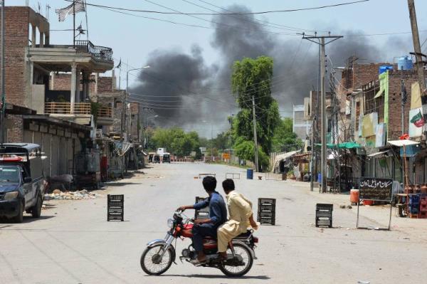 Men riding a bike watch as smoke rises following an explosion allegedly after militants suicide squad attempted to storm an army canto<em></em>nment that houses military residences and offices in Bannu