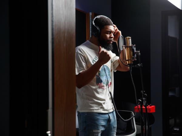Coleman is shown in a studio space in front of a microphone.