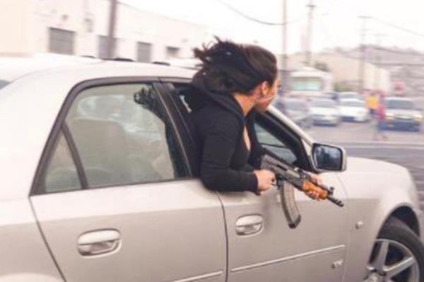 Woman holding an AK-47 leaning out a car window.