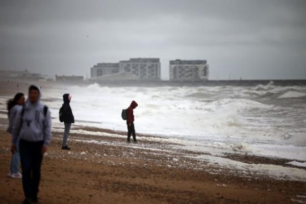 People walk along the beach in Brighton, southern England on August 5, 2023, as Storm Antoni brings rain and high winds to the UK. (Photo by HENRY NICHOLLS / AFP) (Photo by HENRY NICHOLLS/AFP via Getty Images)