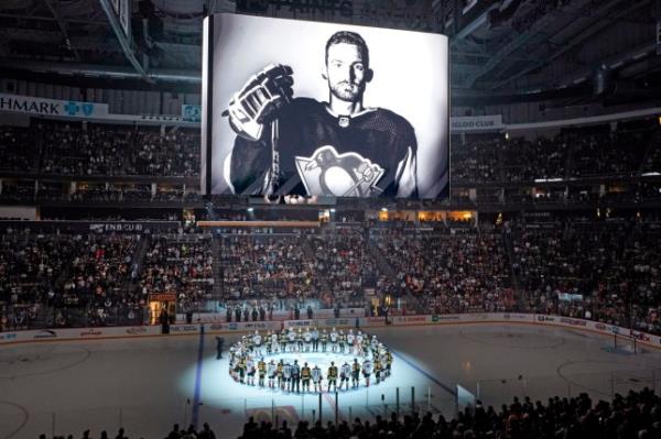 The Pittsburgh Penguins and Anaheim Ducks gather at center ice, before an NHL hockey game in Pittsburgh, Monday, Oct. 30, 2023, to ho<em></em>nor former Penguin player Adam Johnson, shown on scoreboard, who died in while playing in an English hockey league game. (AP Photo/Gene J. Puskar)