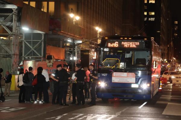 Cops stand in front of parked bus at night to investigate crash.