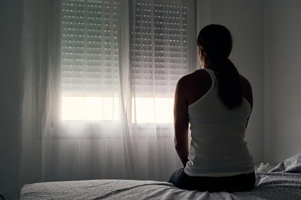 Rear view of an unrecognizable abused woman sitting on her bed looking out the window.