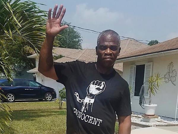 Leo<em></em>nard Cure raises his hand in the air as he wears a t-shirt with an illustration of  raised fist with broken cuff around it and the word 