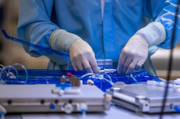 An employee in one of Miltenyi Biotec's clean rooms checks the tightness of a tube set in which patient cells are modified into drugs.