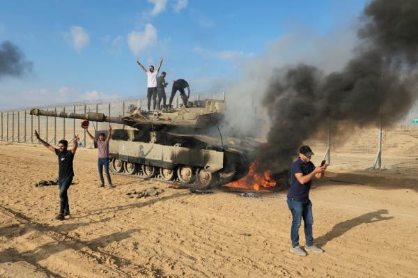 Palestinians celebrate by a destroyed Israeli tank at the Gaza Strip fence east of Khan Younis.