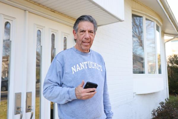 Barry Pollack with cell phone in hand, wearing a blue sweatshirt, outside the door of the Friendly Lane home. 