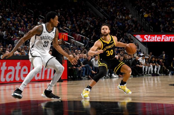 Stephen Curry of the Golden State Warriors handles the ball as Nic Claxton defends.