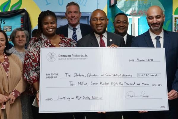 Group shot shows Sheree Gibson and Queens Borough President Do<em></em>novan Richards in a group shot presenting a check to a school at an event.