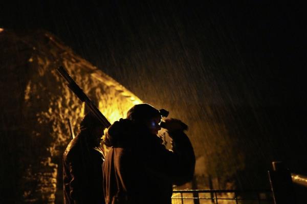 Two rangers on night patrol are seen in silhouette, with the one in the rear carrying a gun and the one in the foreground holding a scope to his eyes.