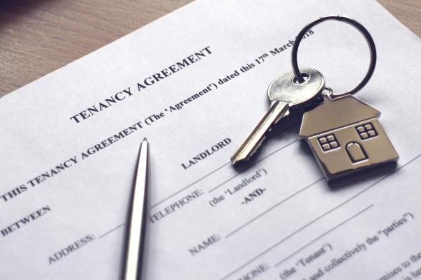 A tenancy agreement paperwork, pen and key attached to a keychain in the shape of a house on top.