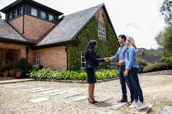 Realtor shakes hands of prospective homeowners in front of house.