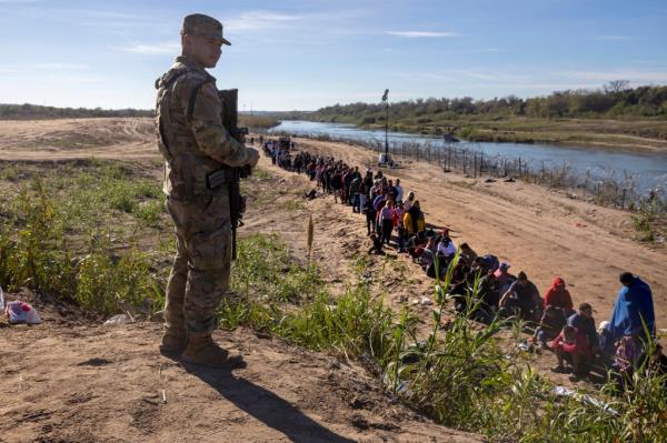 A Texas Natio<em></em>nal Guard soldier watches over a group of more than 1,000 migrants who had crossed the Rio Grande from Mexico on December 18, 2023 in Eagle Pass, Texas.