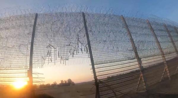 A hole in the border fence with the sun rising in the background. 