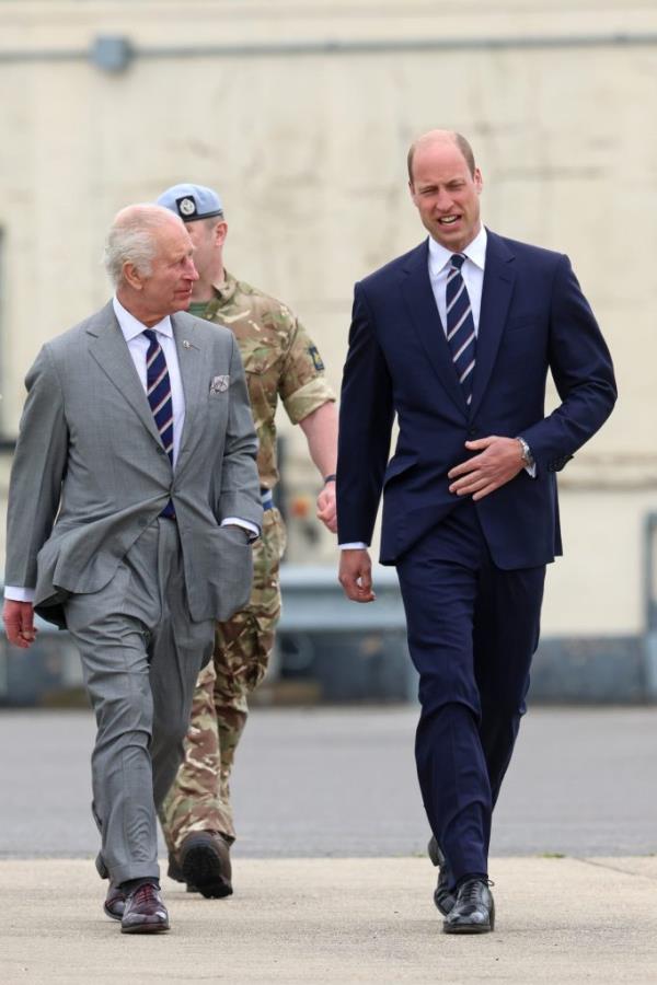 King Charles III and Prince William, both clad in suits, smiling as Charles officially passes the role of co<em></em>lonel-in-Chief of the Army Air Corps to William.