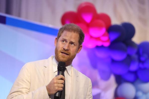 Prince Harry, Duke of Sussex, delivering a speech at the Nigerian Defence Headquarters in a white suit, holding a microphone