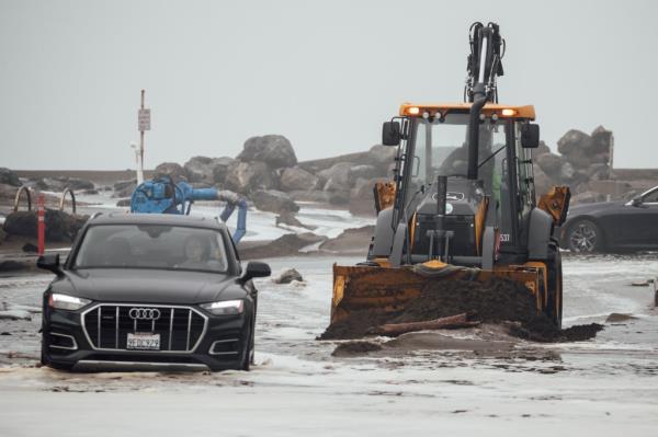 A front end loader removes debris along a flooded Clarendon road due to high waves in Pacifica, Calif., on Dec. 28, 2023.