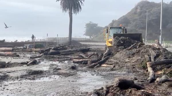 A heavy machinery clears mud and fallen trees off the beach, as massive waves hit the California coastline, in Santa Cruz county, Calif. on Dec. 28, 2023. 
