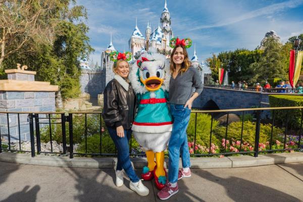 Hilary Duff and Mandy Moore posing with Daisy Duck in front of Sleeping Beauty's Winter Castle at Disneyland in California.