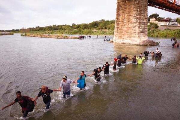 Migrants hold hand while crossing the Rio Grande river from Mexico into Eagle Pass, Texas.