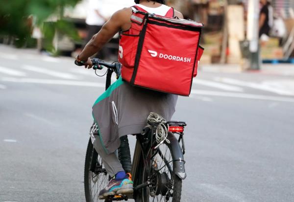 A man rides a red bicycle with a Door Dash bag on the back in New York City.