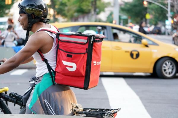 A person delivering food on an electric bike with a Door Dash bag on the handlebar.