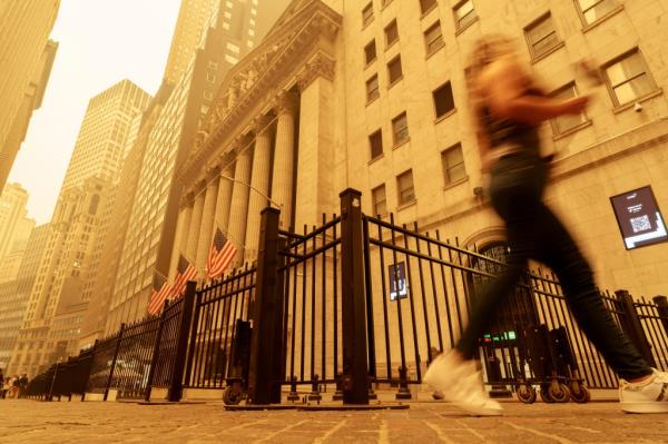 A pedestrian walks past the smoke and haze shrouded New York Stock Exchange building in New York City Wednesday, June 7, 2023. 