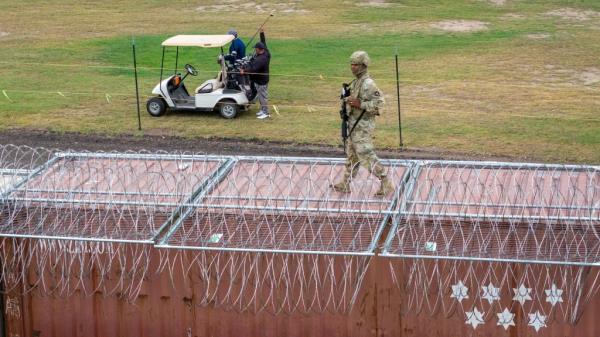 In an aerial view, a Texas Natio<em></em>nal Guard soldier stands atop a barrier of shipping co<em></em>ntainers and razor wire while guarding the U.S.-Mexico border