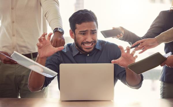 A man looks stressed at his computer as multiple people demand his attention.
