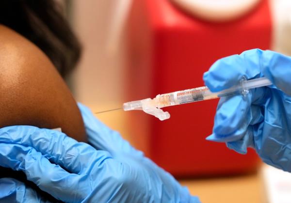 A hand holding a needle a<em></em>bout to inject a COVID-19 vaccine in a person's shoulder.