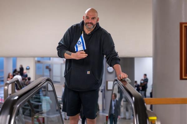 Senator John Fetterman holding a small Israel flag heading to the chamber for a vote at the Capitol in Washington, 2024.