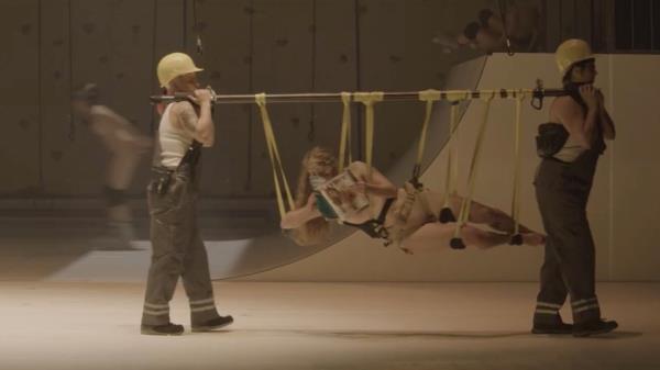 A naked woman being carried on a stick hanging on straps