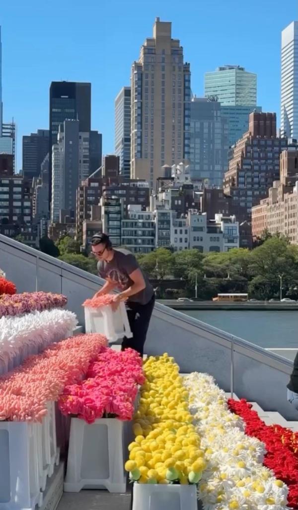A New York Police Department officer standing in front of a large white tent filled with plush flowers at the Flower Market exhibition, asking people to leave due to overcrowding.