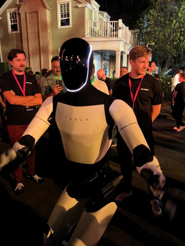 Optimus bot gesturing to human with bent legs at event on Oct. 10, 2024.
