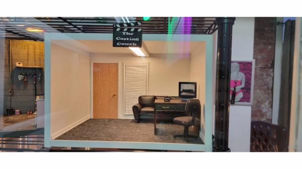 A miniature set with a couch, table, computer, camera, chair, window with blinds, and a door. 