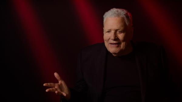 Steve Binder in a recent photograph taken from the Paramount+ docu<em></em>mentary a<em></em>bout the Elvis comeback special. He's got grey hair, is wearing all-black and is gesticulating with his right hand as if he's making a point.