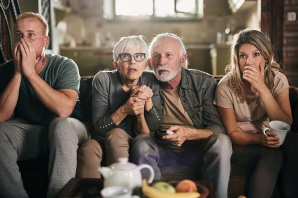Two men and two women anxiously watching TV.