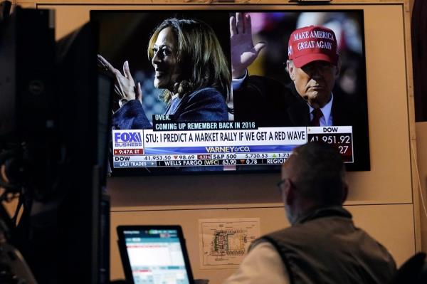 The back of a man's head is visible as he watches TV with a split screen of Kamala Harris and Do<em></em>nald Trump/