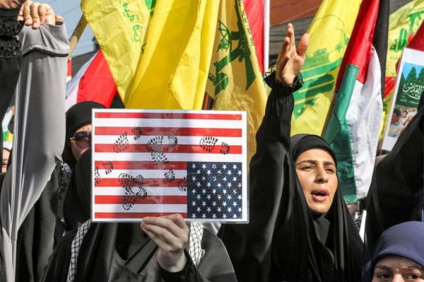 A woman holds a sign showing a US flag defaced by boot foot prints before Palestinian and Hezbollah flags during an anti-Israel rally