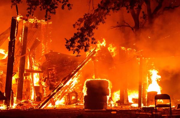 A pile of tires and the wooden from of a property in Tehama County, California is seen engulfed in flames, with more flames and heavy smoke from the Park wildfire in the background on July 26.