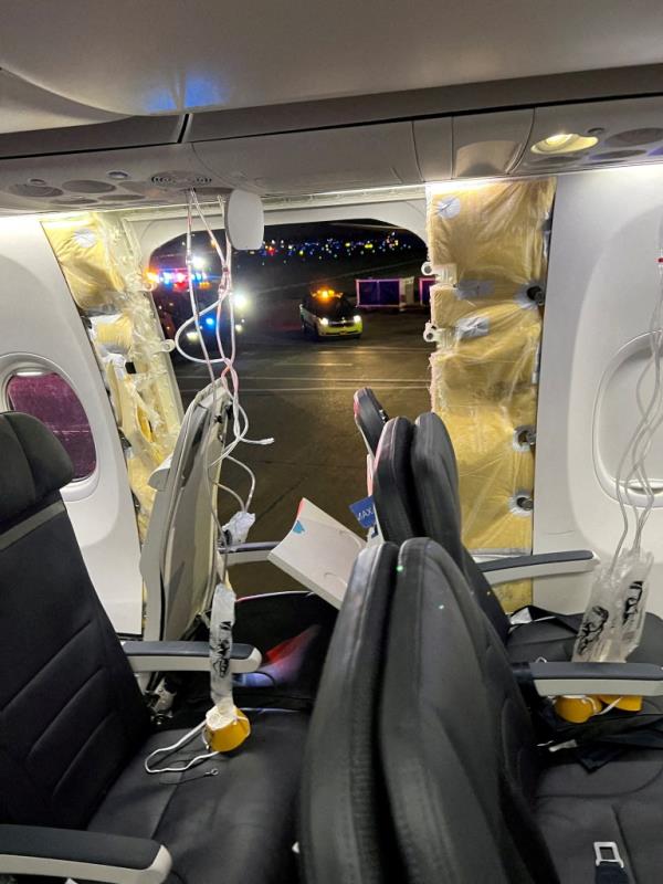 Passenger oxygen masks hang from the roof next to a missing window and a portion of a side wall of an Alaska Airlines Flight 1282.
