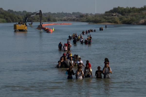 A caravan wades past a string of buoys, being co<em></em>nstructed to deter migrants crossings through the Rio Grande river, as they look for an opening in the co<em></em>ncertina wire to enter into Eagle Pass, Texas, U.S. July 27, 2023.