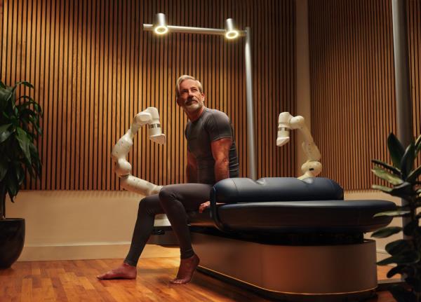 A man sitting on a bed with robotic arms for Aescape Hero press photos