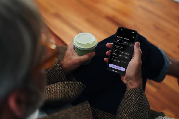 A person holding a phone with Aescape App booking screen displayed, and a cup of coffee