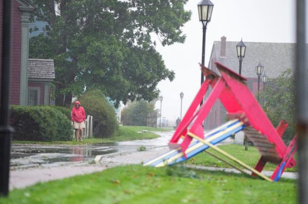 A man stands on a rain-soaked street looking at a very large Adiro<em></em>ndack chair   that was overturned by the storm.