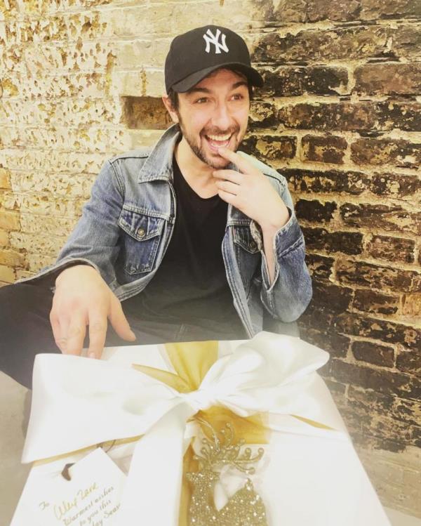 Alex Zane smiling with a large box. 