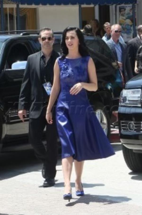 Aaron Cohen wearing all black walking behind Katy Perry wearing a purple midi dress. 