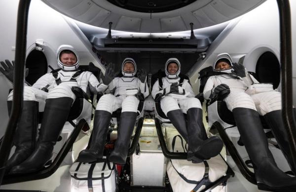 Roscosmos cosmo<em></em>naut Alexander Grebenkin, left, and NASA astro<em></em>nauts Michael Barratt, Matthew Dominick and Jeanette Epps inside the SpaceX Dragon Endeavour spacecraft seen in space gear smiling and waving.