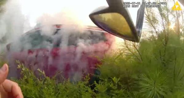 Red car with smoke coming out of it in wooded area. 