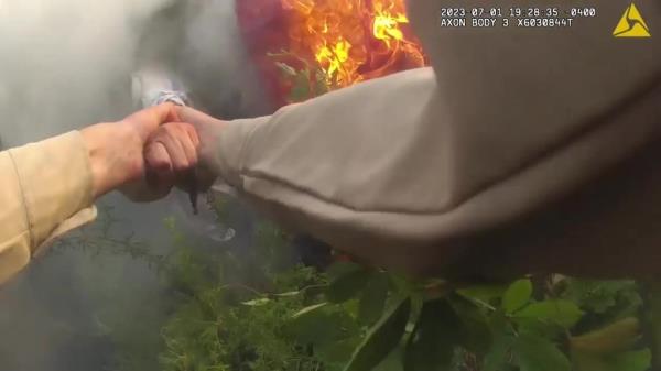 Deputy's hands outstretched and grabbing o<em></em>nto hand of person from inside car covered in flames and smoke. 